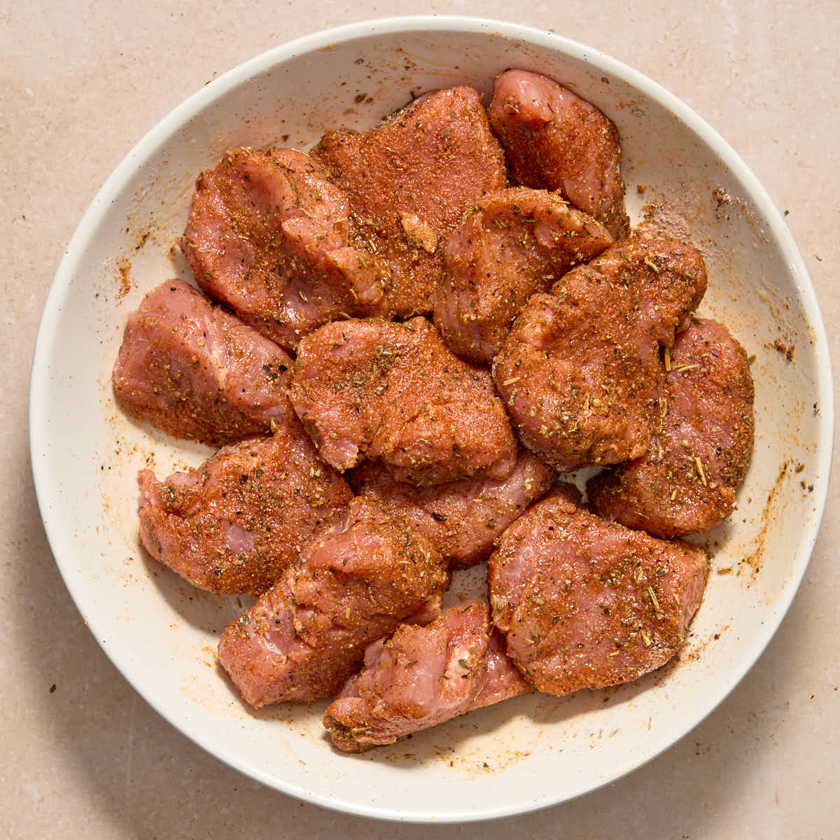 Sliced pork tenderloin coated in seasoning in a white bowl.