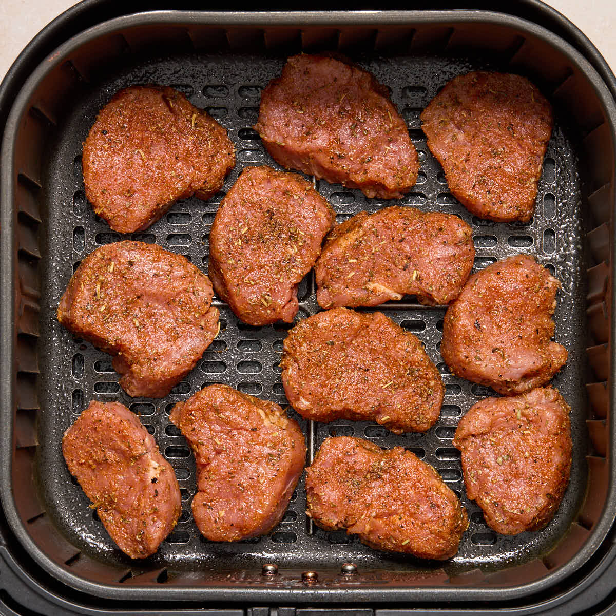 Seasoned, raw pork medallions arranged in a single layer in the air fryer basket.