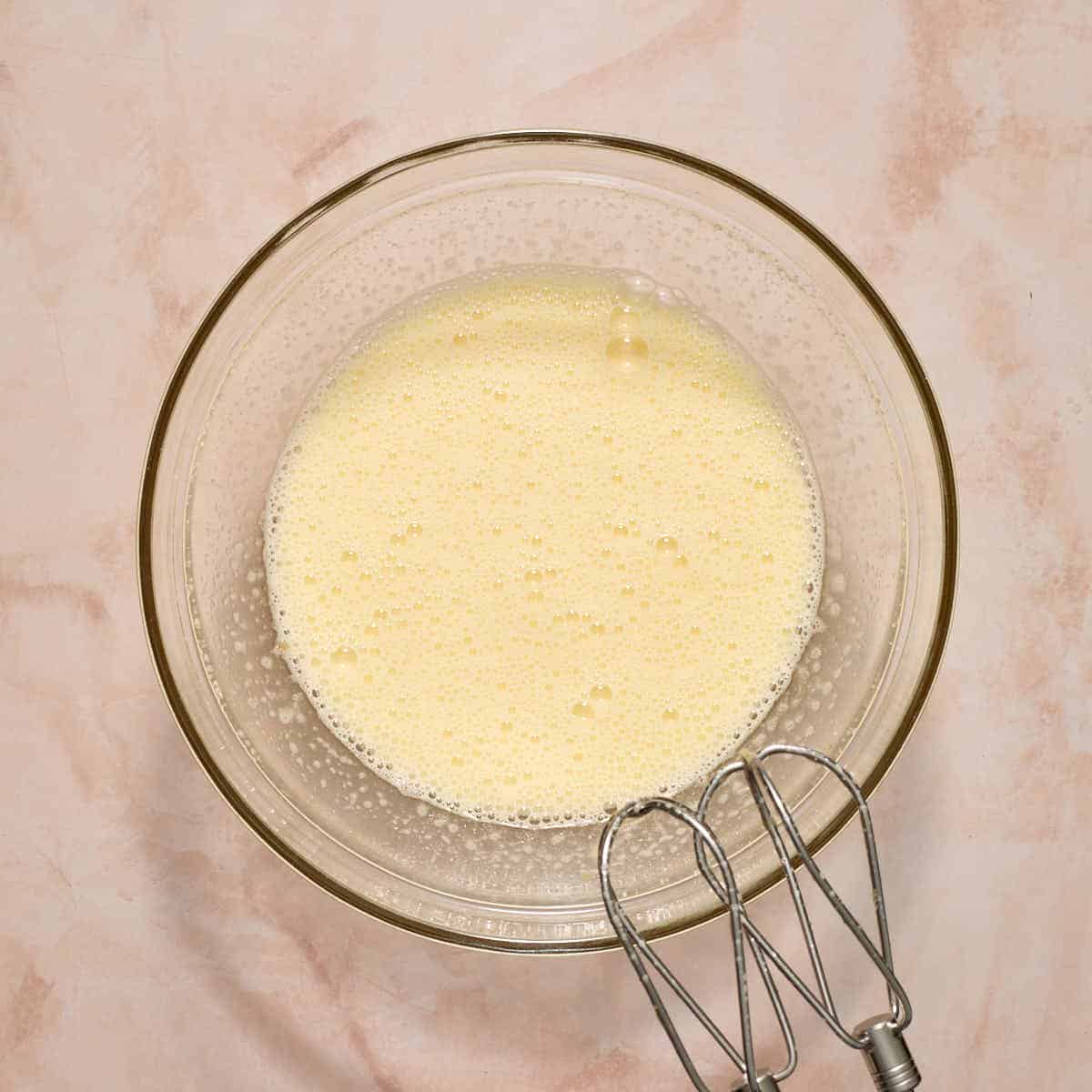 Eggs and sugar beaten together in a glass bowl with an electric mixer.