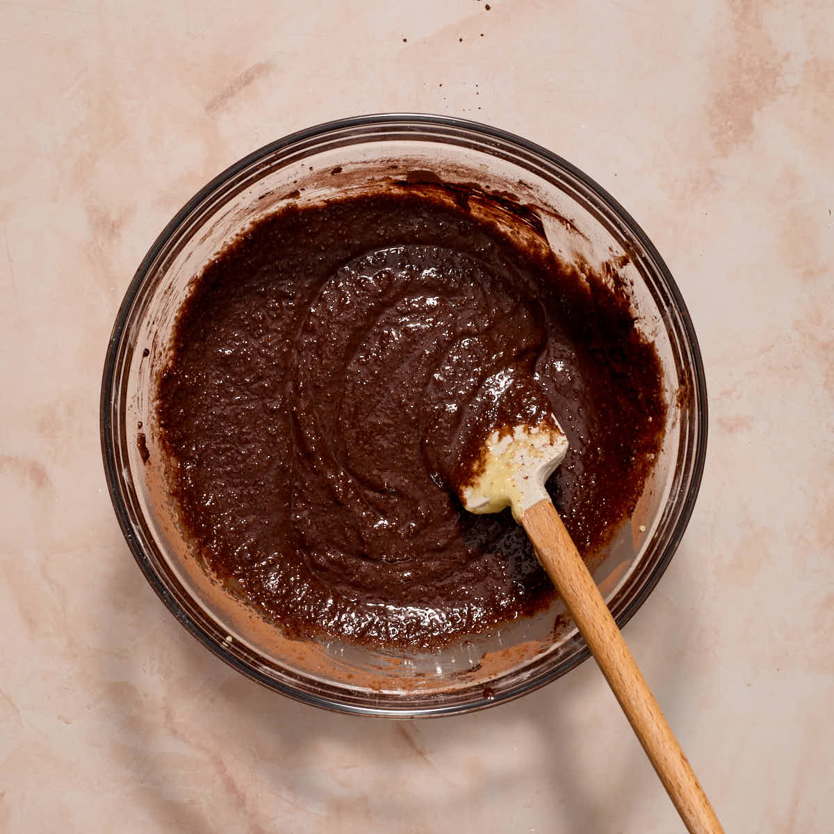 Chocolate batter mixed together with a spatula in a glass bowl.