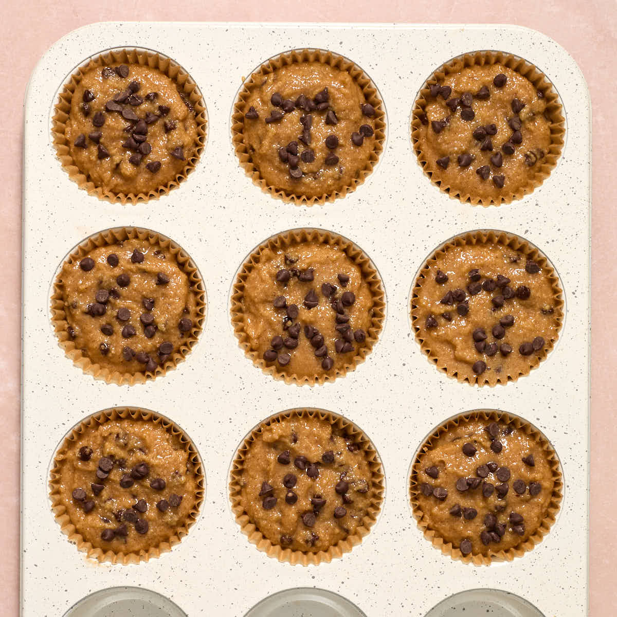 Muffin batter scooped into the prepared muffin pan with extra chocolate chips placed on top.