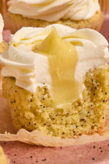 A lemon poppy seed cupcake with some removed to show the lemon curd filling inside.