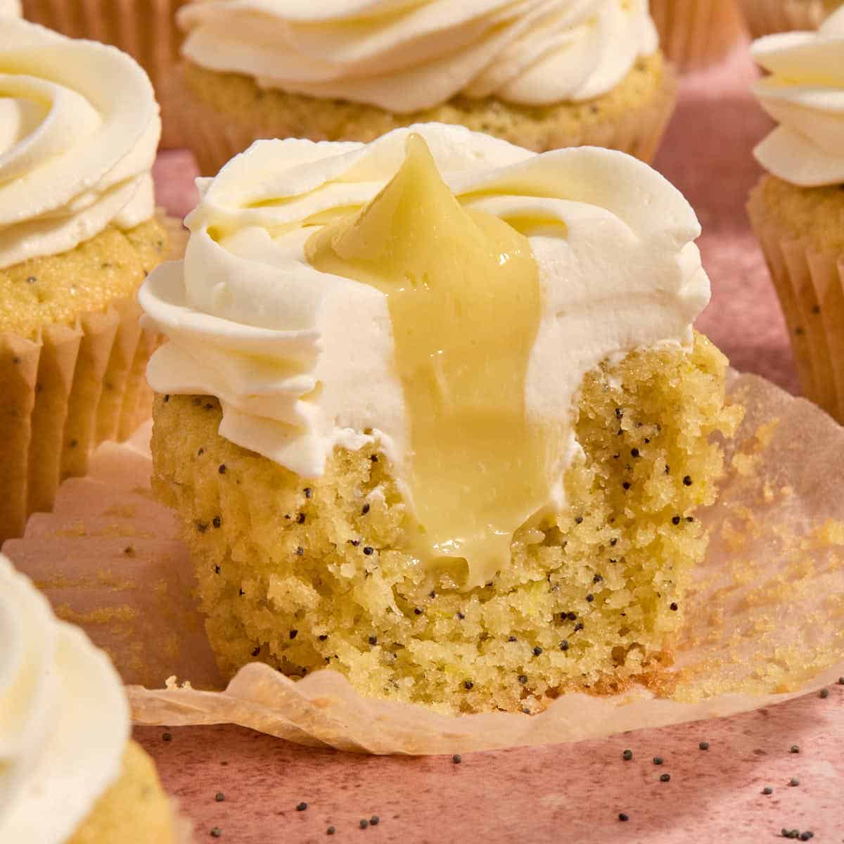 A lemon poppy seed cupcake with some removed to show the lemon curd filling inside.