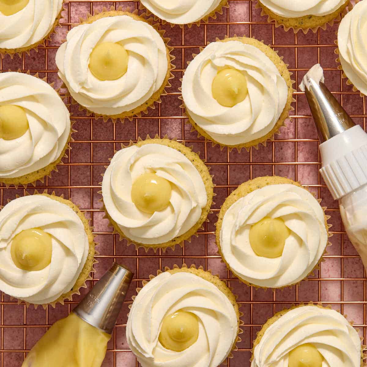 Whipped cream piped onto cupcakes with more lemon curd piped on top.