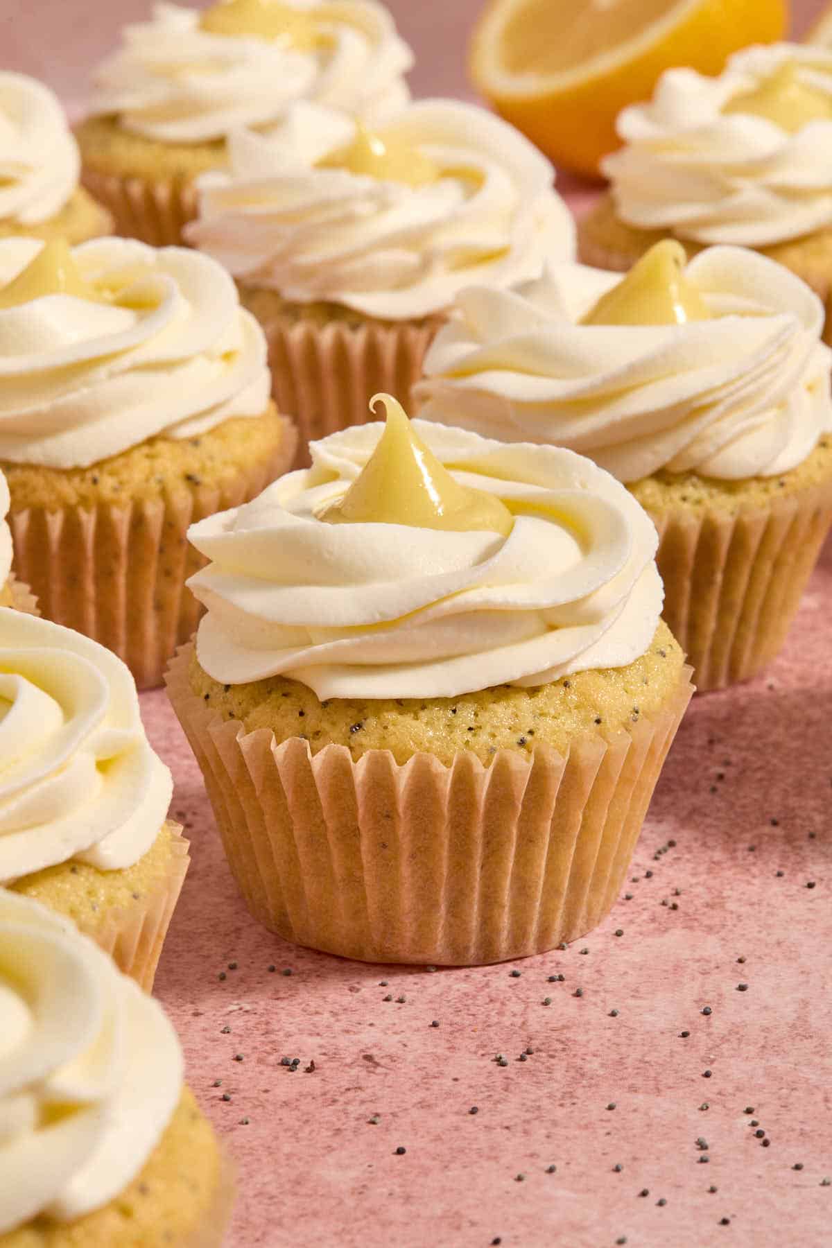 A bunch of cupcakes arranged on a pink surface.