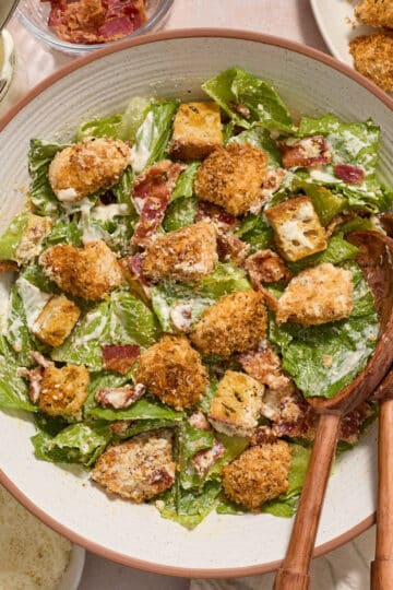 Air fryer chicken caesar salad served in a bowl with wooden serving spoons.