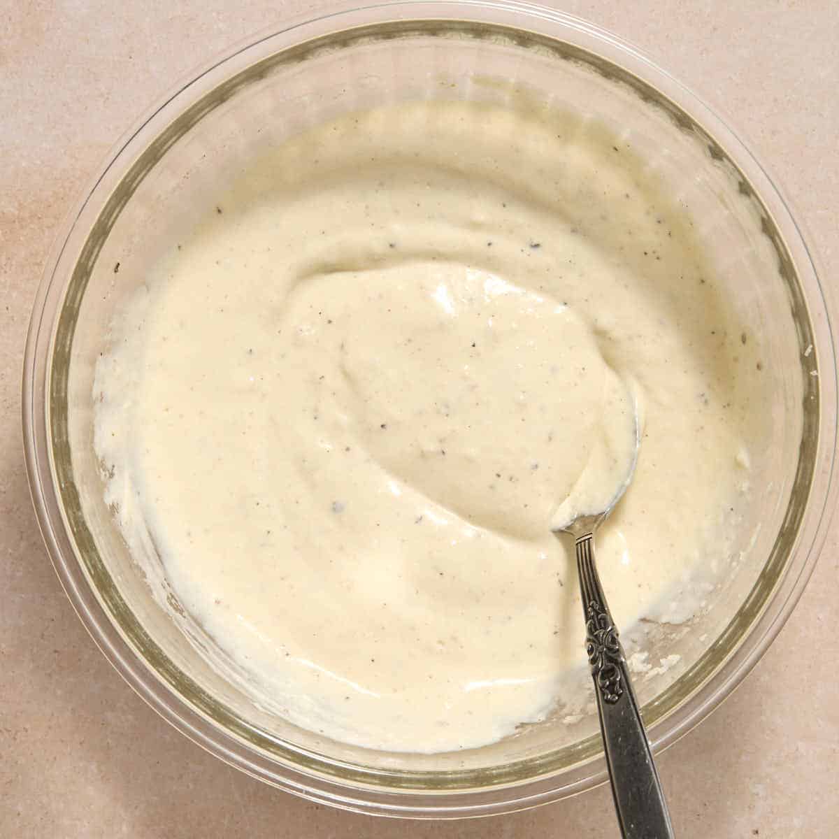 Caesar dressing in a small bowl with a spoon.