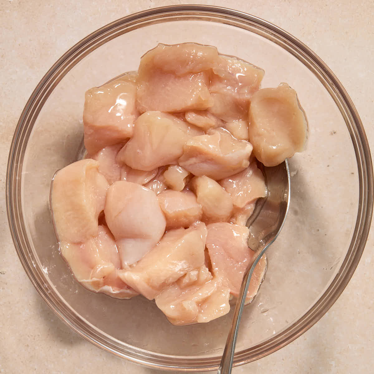 Cubed chicken in a bowl and coated with oil.