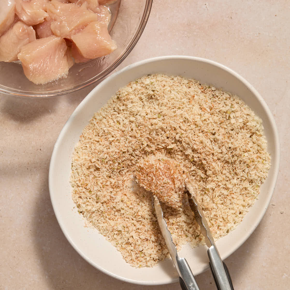 Piece of chicken being rolled in seasoned panko crumbs.