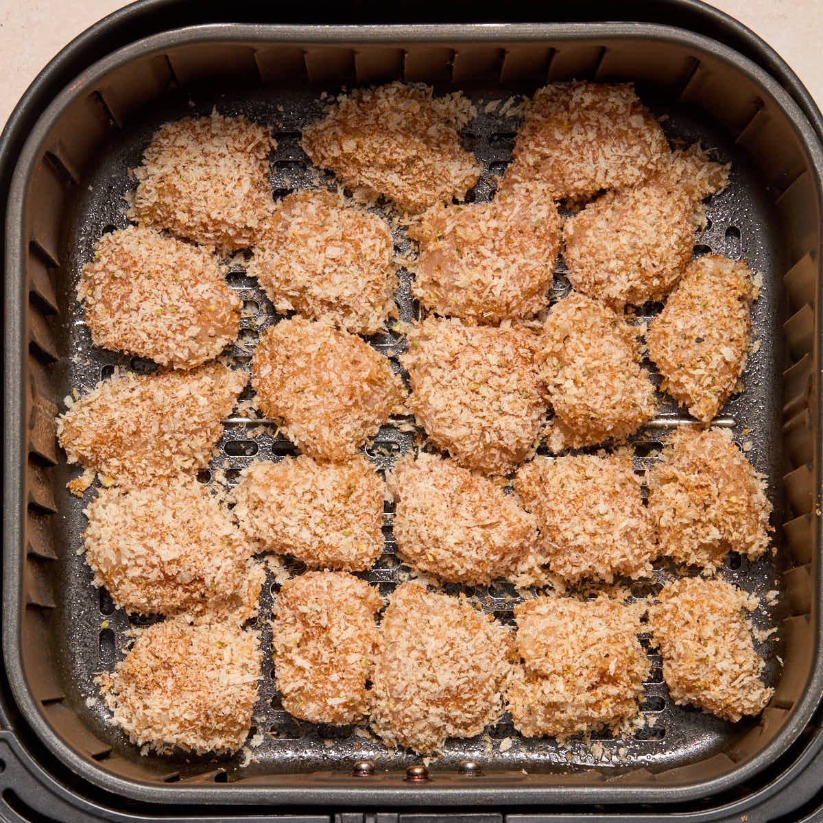 Breaded chicken bites in the air fryer basket before air frying.