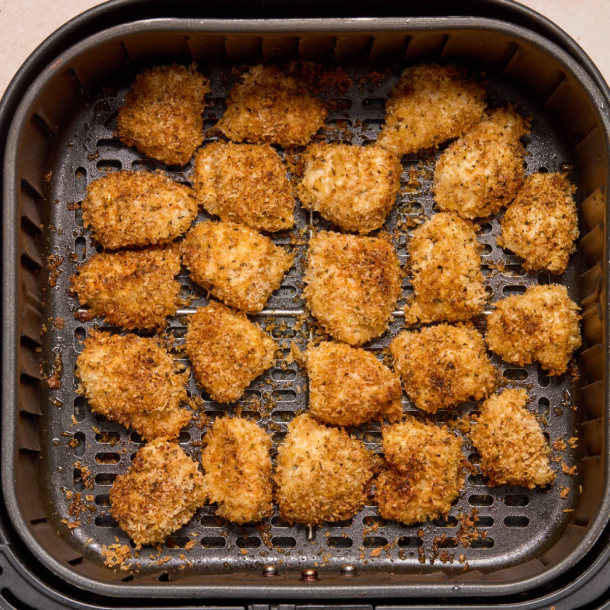 Golden brown air fried chicken bites in the air fryer basket.