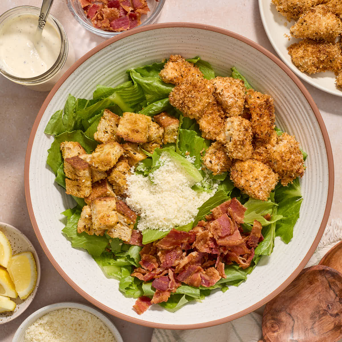 Ingredients for the chicken caesar salad added to a large white bowl with a jar of caesar dressing on the side.