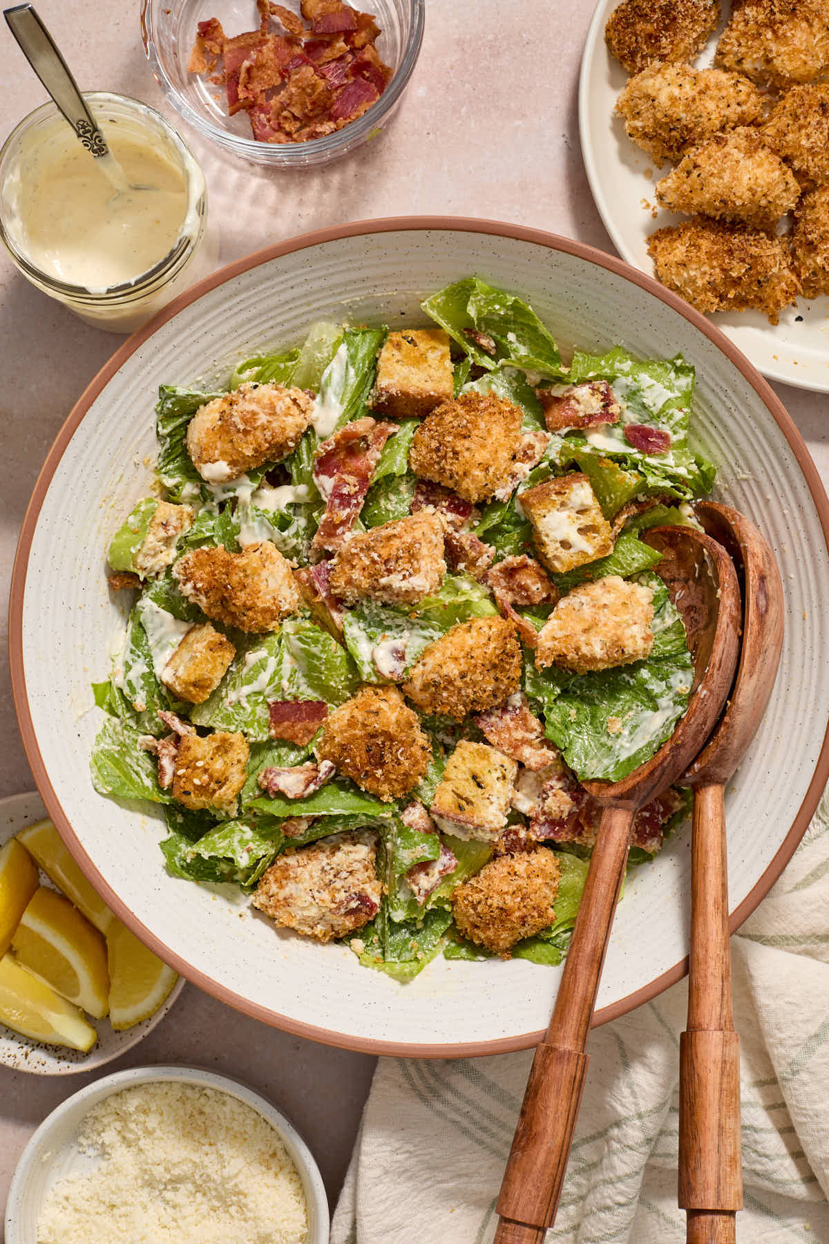 Chicken caesar salad in a white bowl with wooden salad servers.