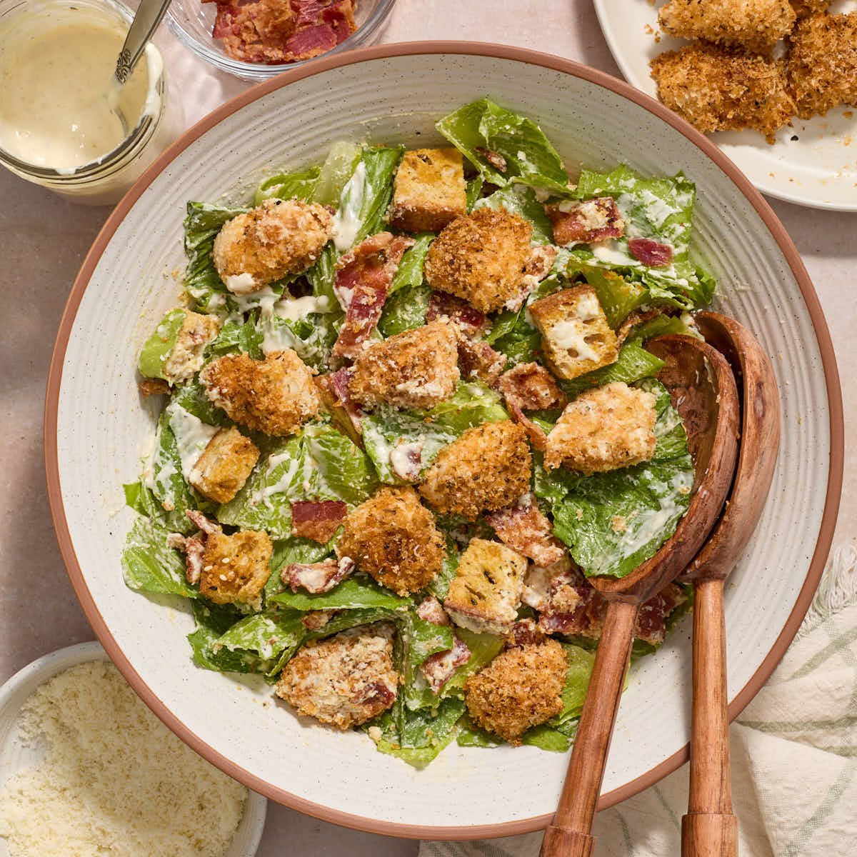 Air fryer chicken caesar salad served in a bowl with wooden serving spoons.