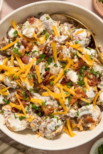 Air fryer potato salad in a white bowl with a serving spoon inserted into it.