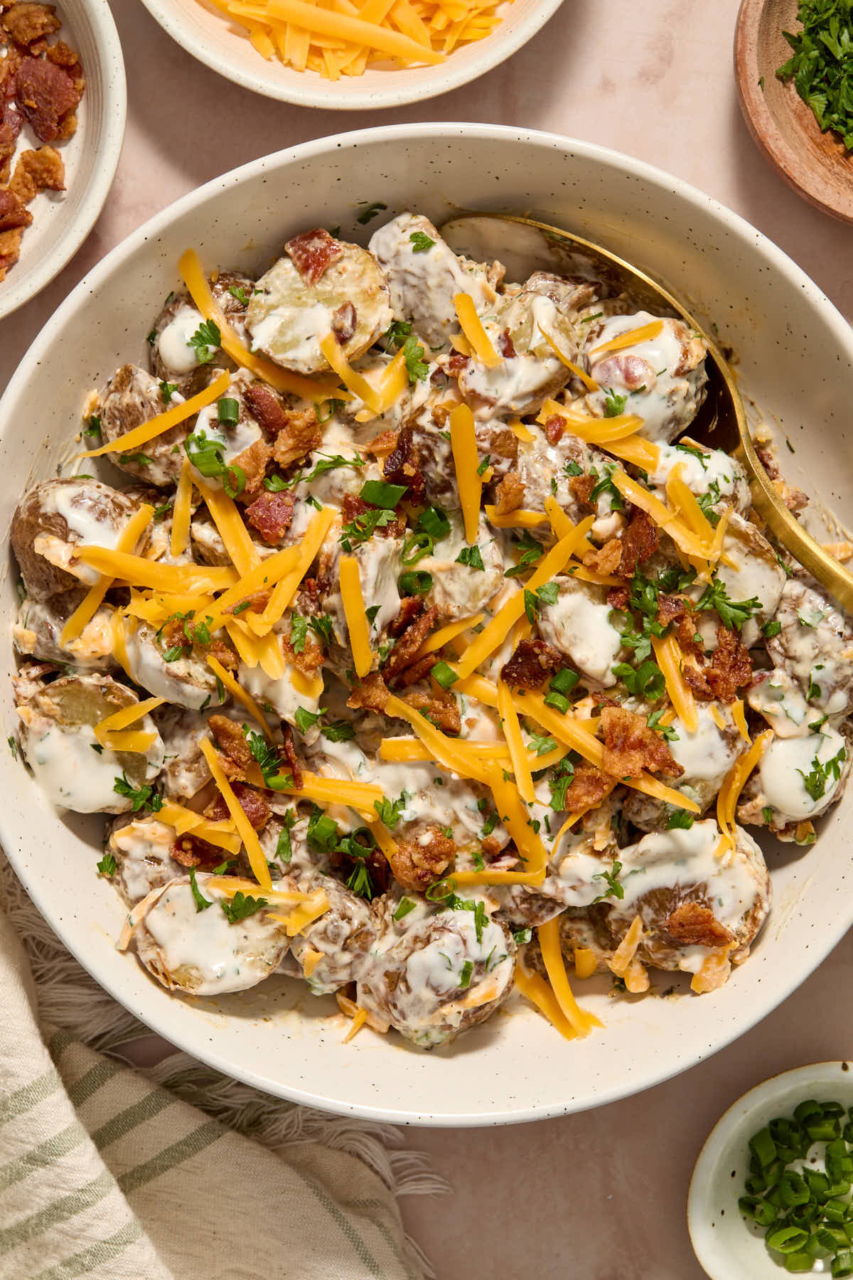 Potato salad topped with cheese, bacon and herbs in a white bowl.