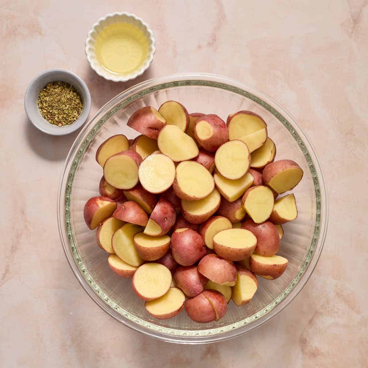 Halved baby red potatoes in a bowl with oil and Italian seasoning on the side.