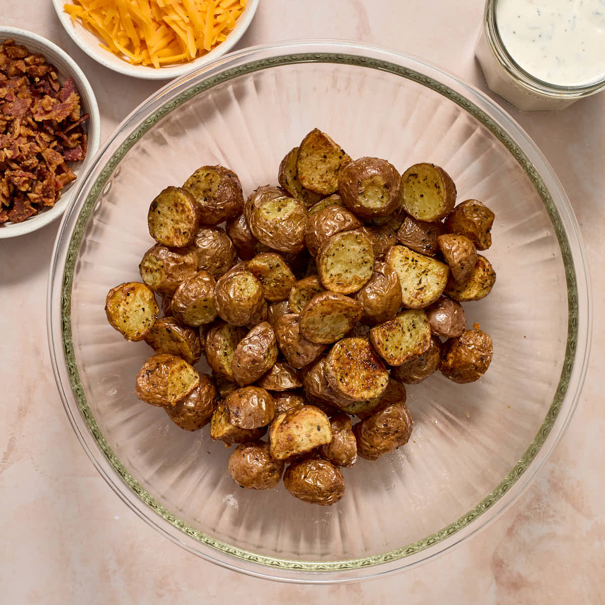 Air fried potatoes in a large bowl with bacon, cheese and ranch dressing on the side.