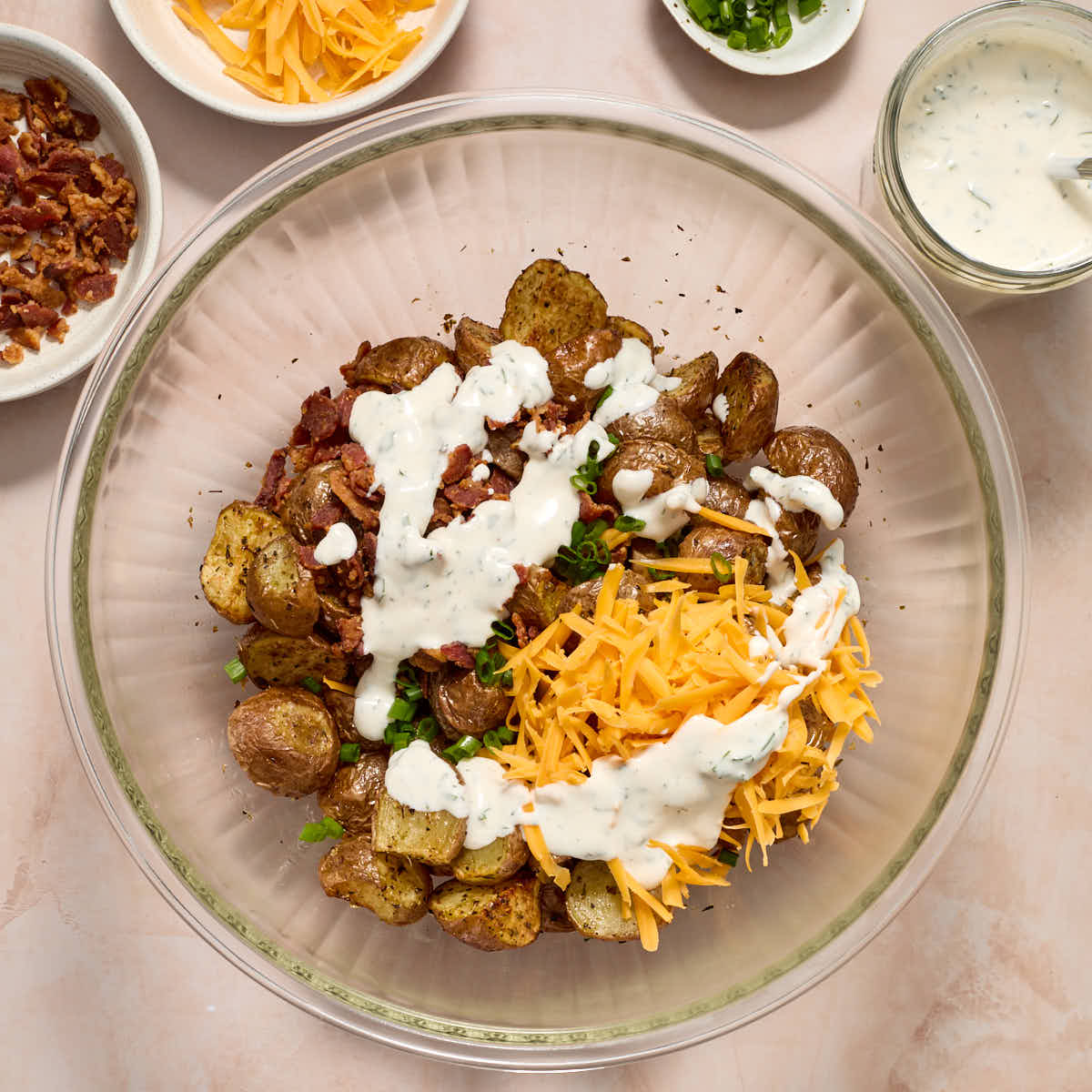 Air fried potatoes in a glass bowl with bacon, cheese, chives and ranch dressing on top.