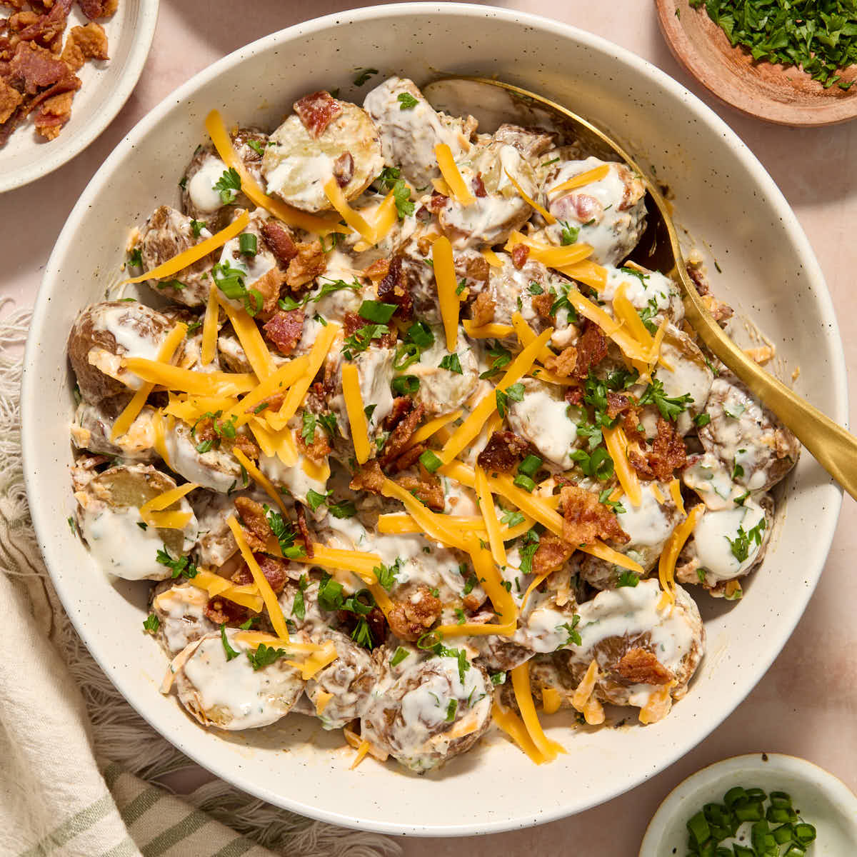 Air fryer potato salad in a white bowl with a serving spoon inserted into it.