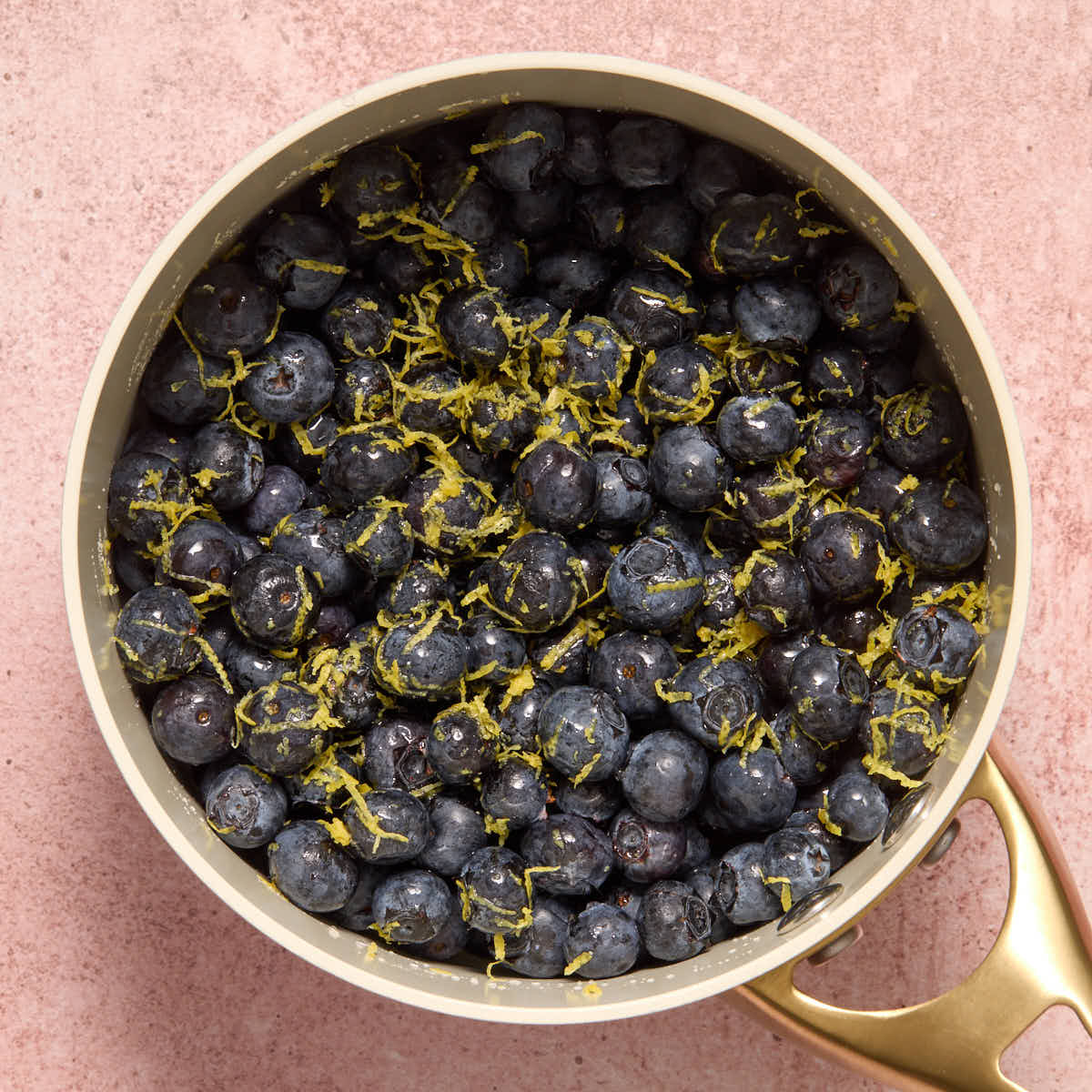 Blueberries in a small sauce pan, mixed with lemon zest, juice and maple syrup.