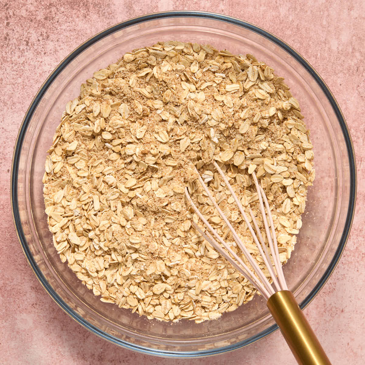 Oats and other dry ingredients whisked together in a glass bowl.