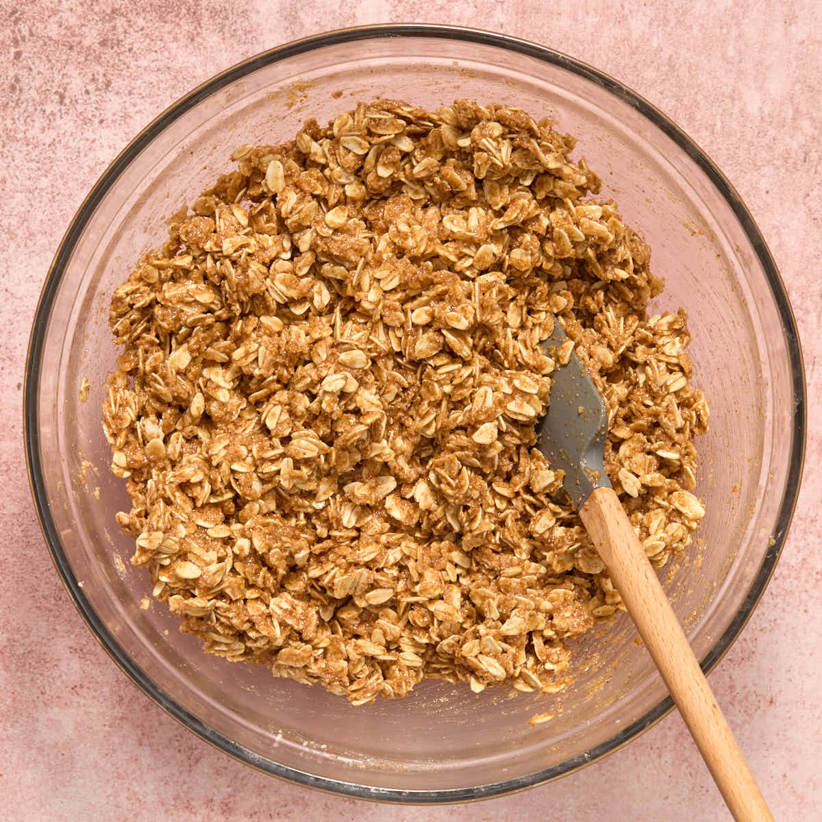 Oat mixture mixed with the almond butter mixture in a glass bowl with a spatula.