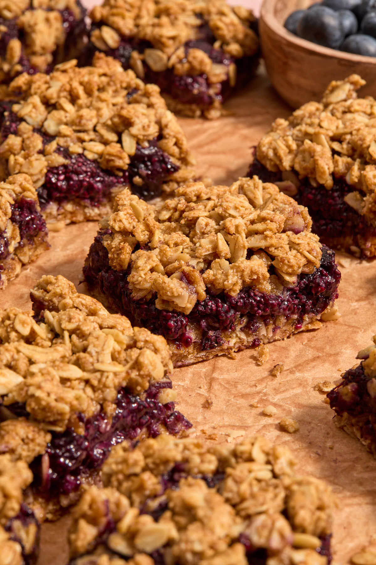 Blueberry bars on crumpled parchment paper with a bowl of blueberries in the background.