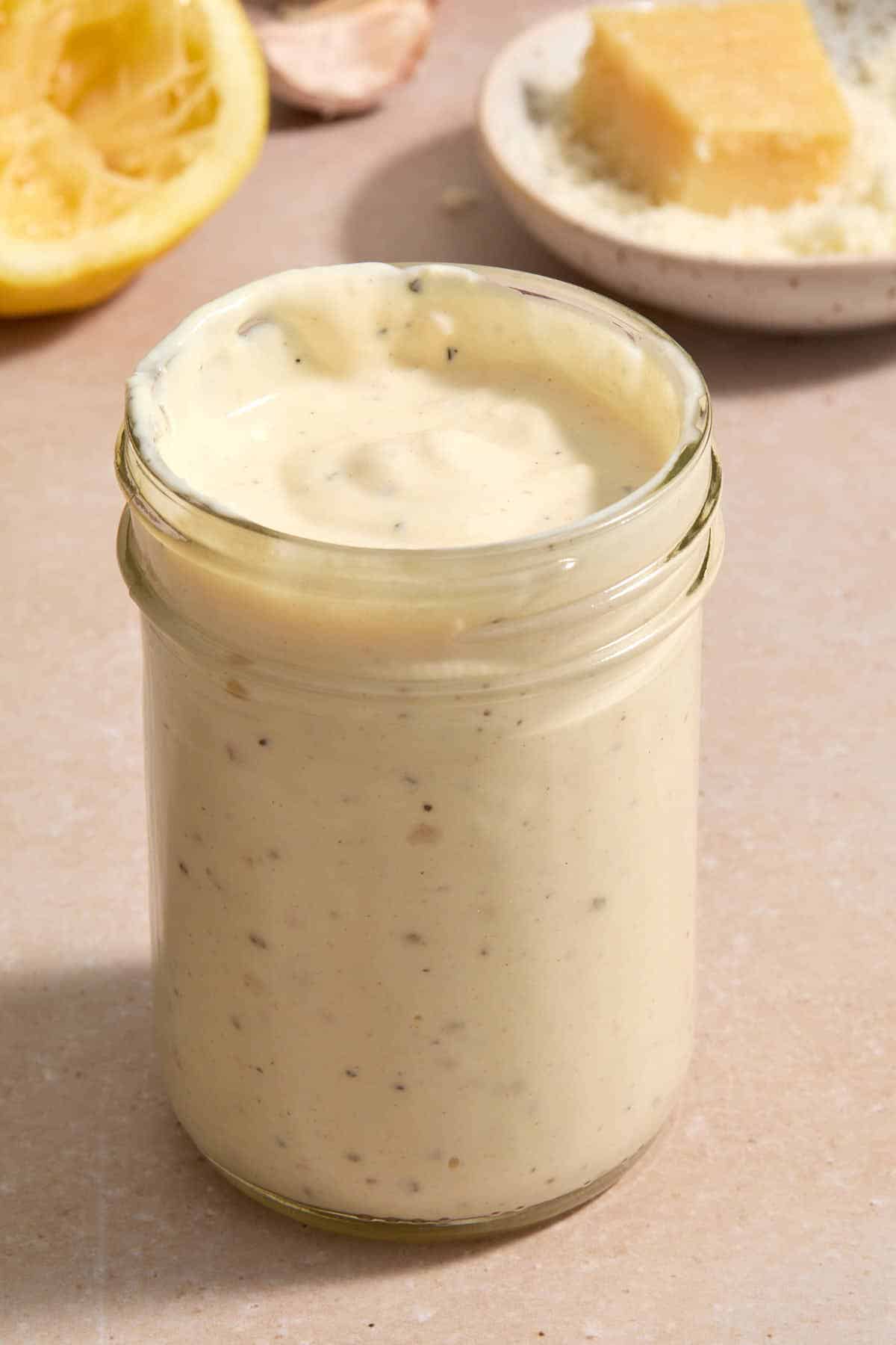 Dressing in a glass jar with lemon and parmesan in the background.