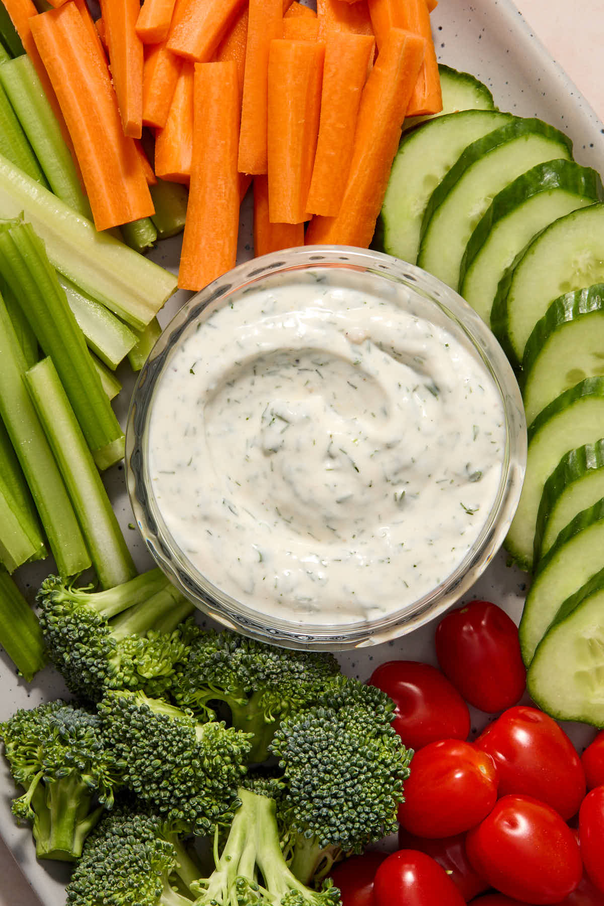 Ranch dressing in a glass bowl, served on a platter with chopped veggies.