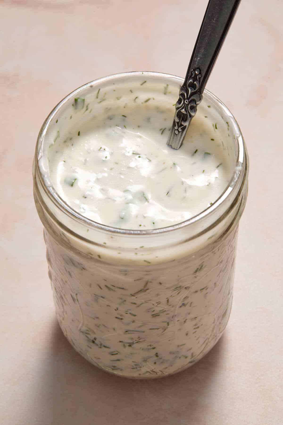 Ranch dressing in a glass jar with a spoon inserted into it.