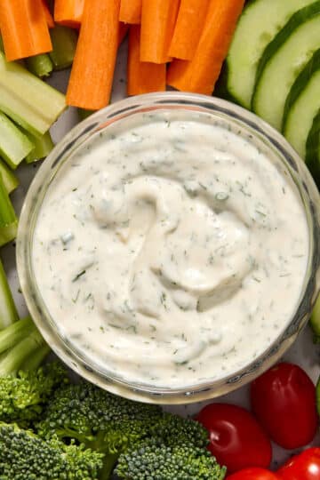 Ranch dressing in a glass bowl and surrounded by chopped veggies.