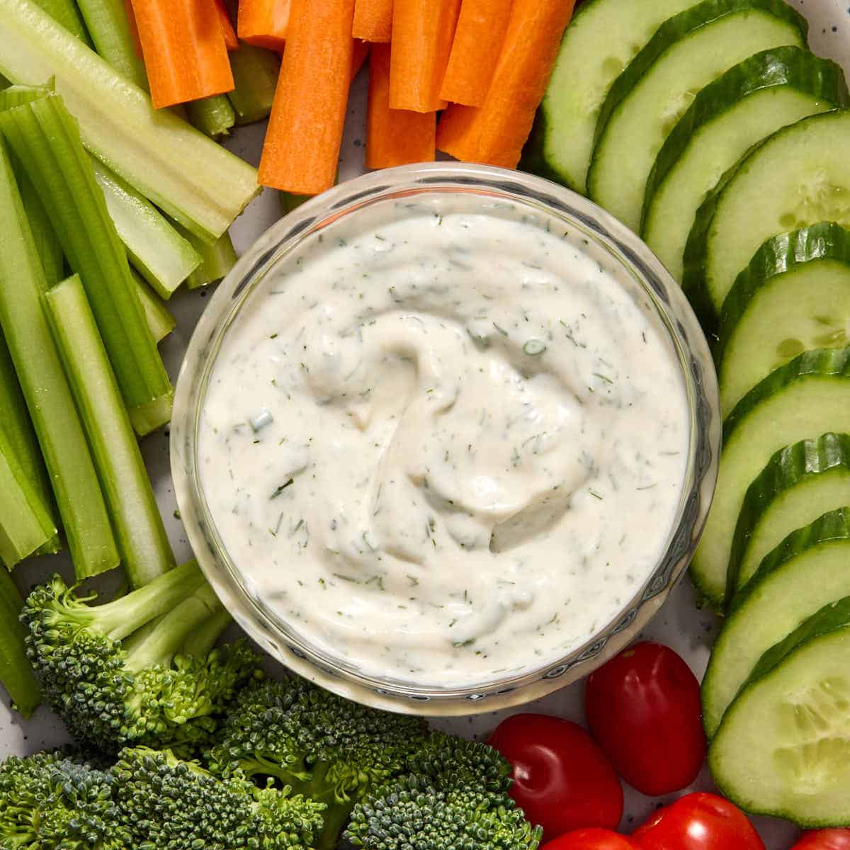 Ranch dressing in a glass bowl and surrounded by chopped veggies.