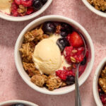 Air fryer berry crisp in a white ramekin with a spoon inserted and a scoop of ice cream on top.
