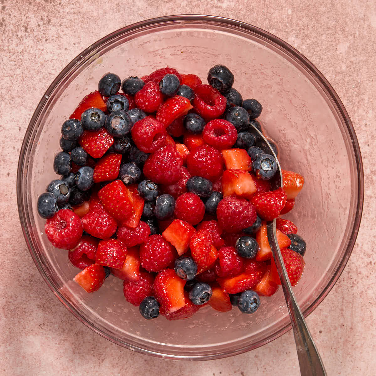 Berry mixture stirred together in a glass bowl with a spoon.