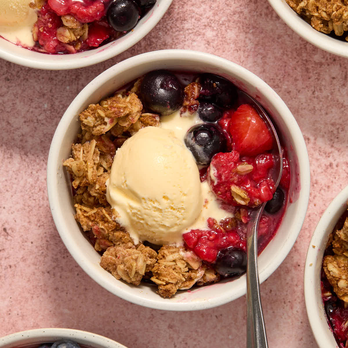 Air fryer berry crisp in a white ramekin with a spoon inserted and a scoop of ice cream on top.