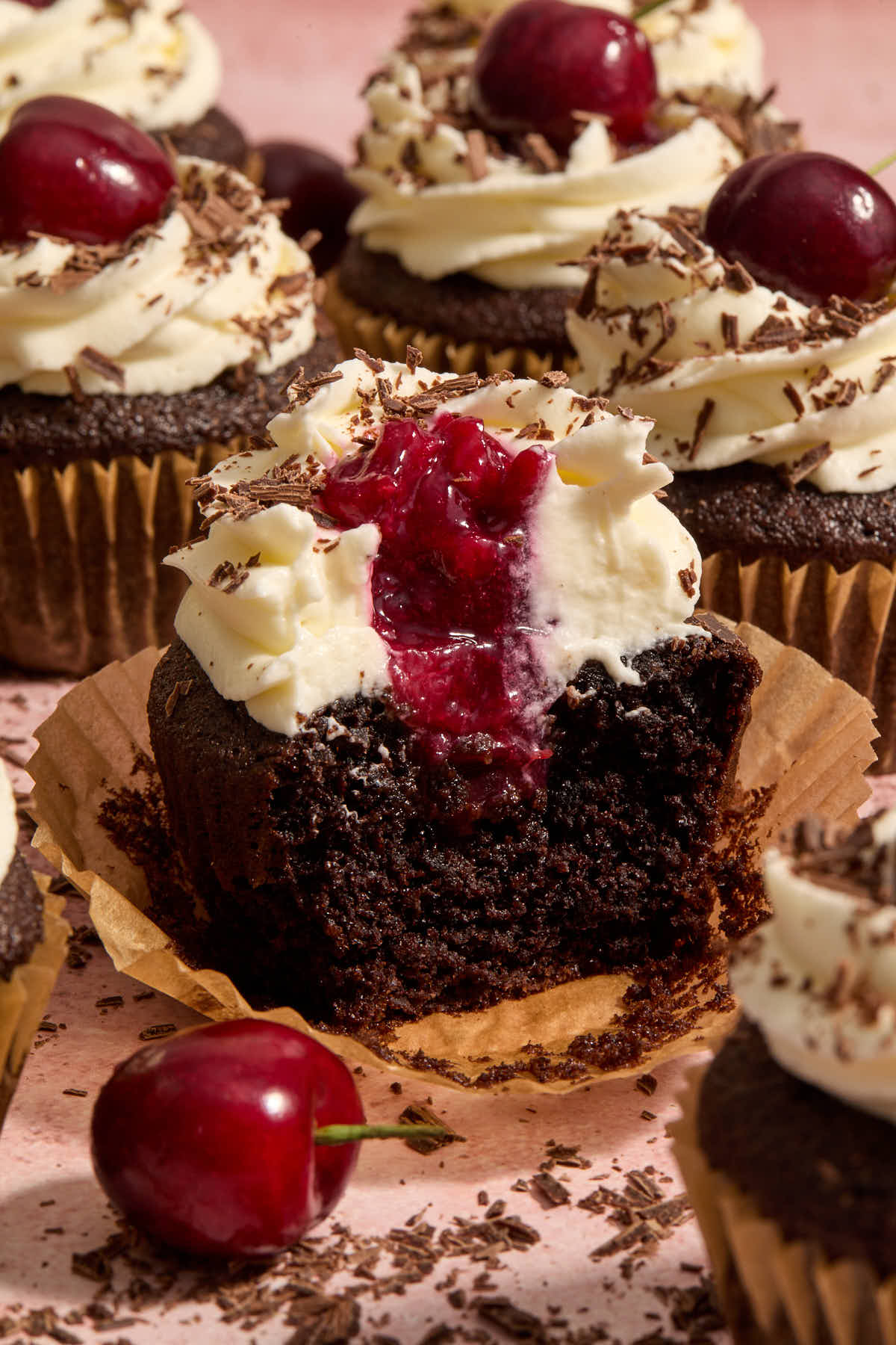 Cupcake cut in half on a parchment cupcake liner, showing the cherry filling inside.