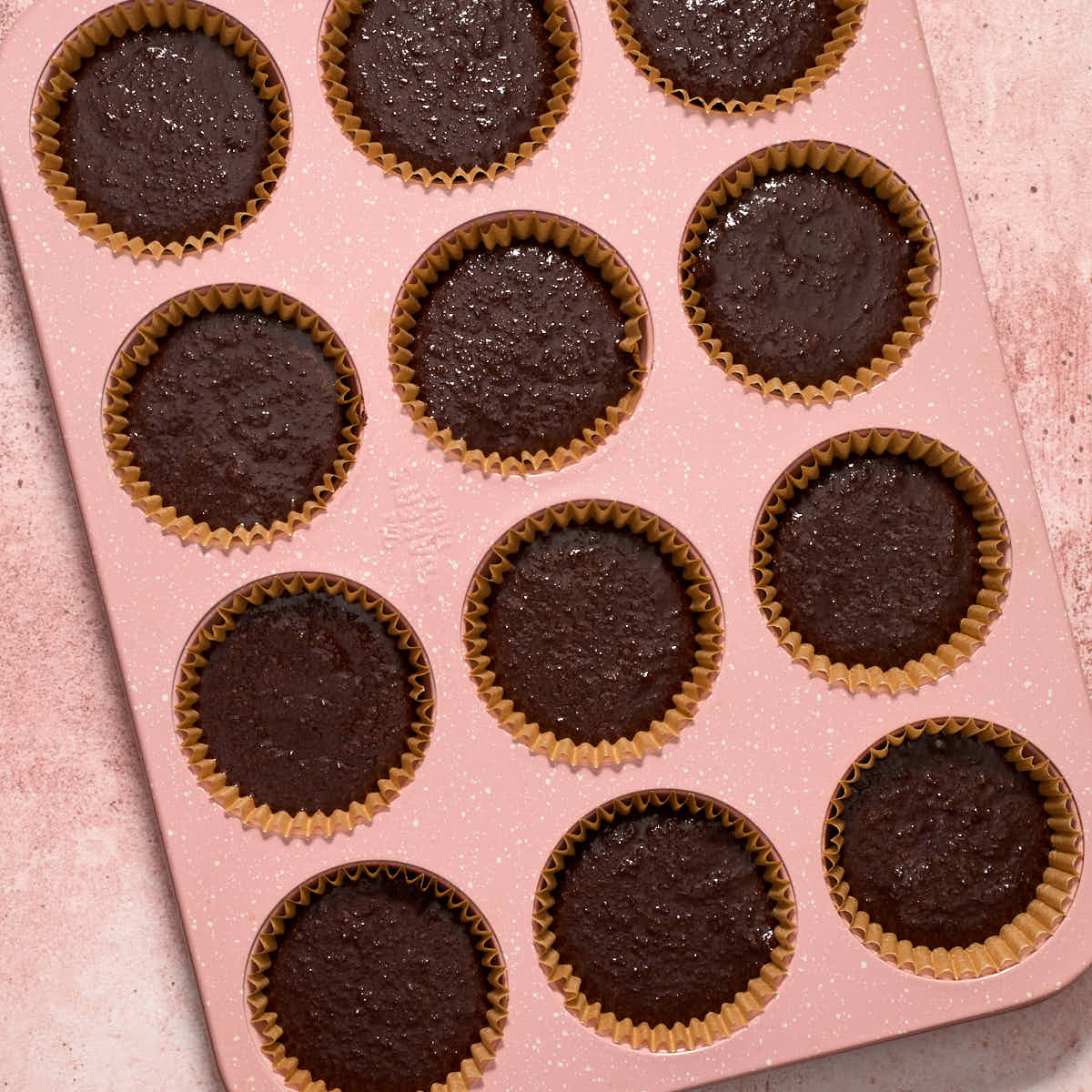 Chocolate cupcake batter added to a cupcake pan with parchment liners.
