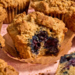 Almond flour blueberry coffee cake muffin with a bite removed and resting on a parchment muffin liner.