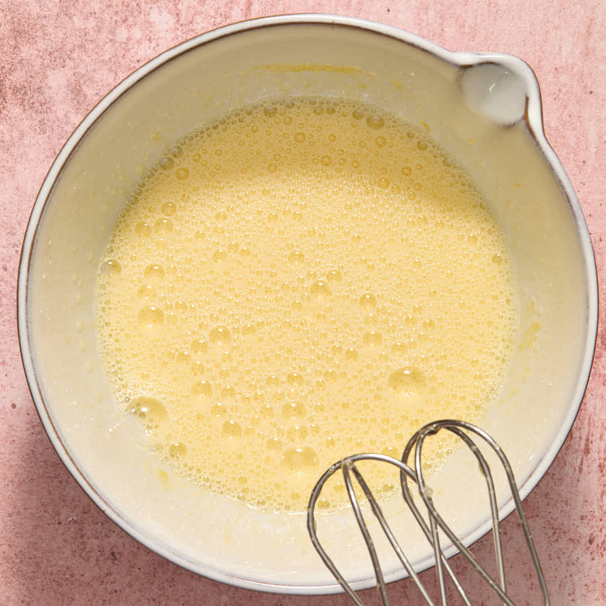 Eggs and sugar beaten together in a white bowl until foamy.