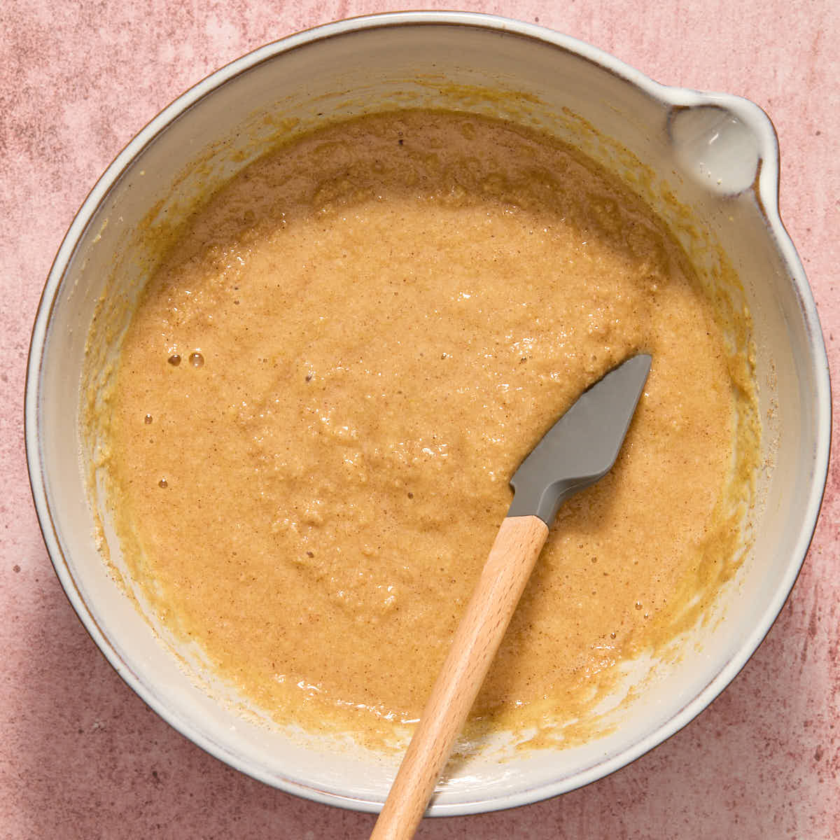 Dry ingredients stirred into the wet ingredients in a white bowl with a spatula.