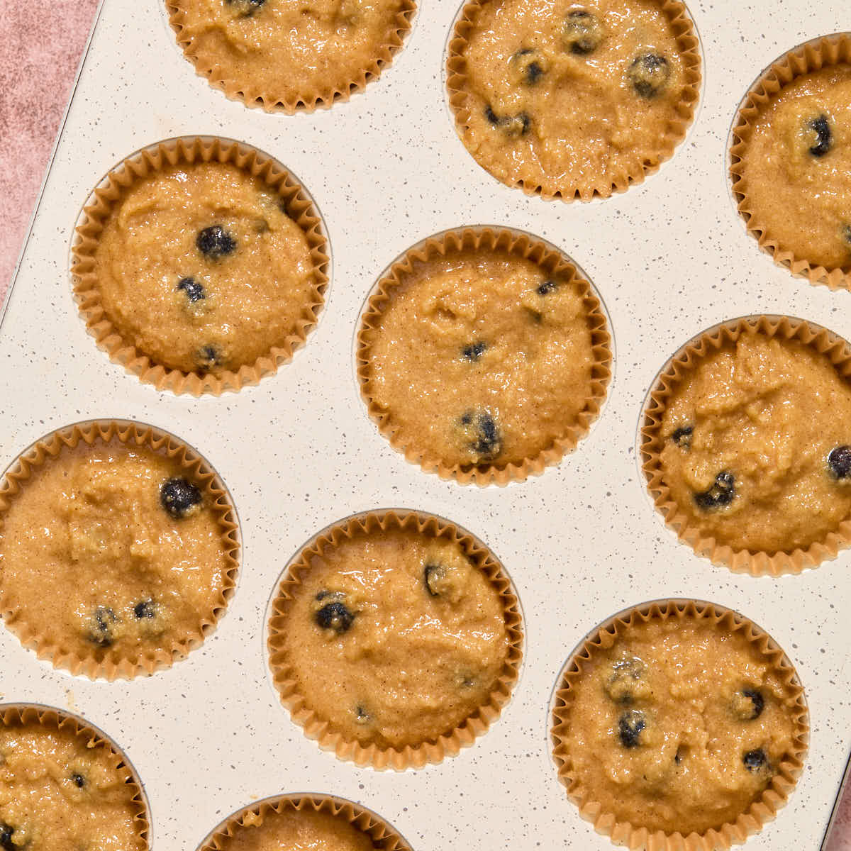 Muffin batter divided into a 12-cavity muffin pan with muffin liners.