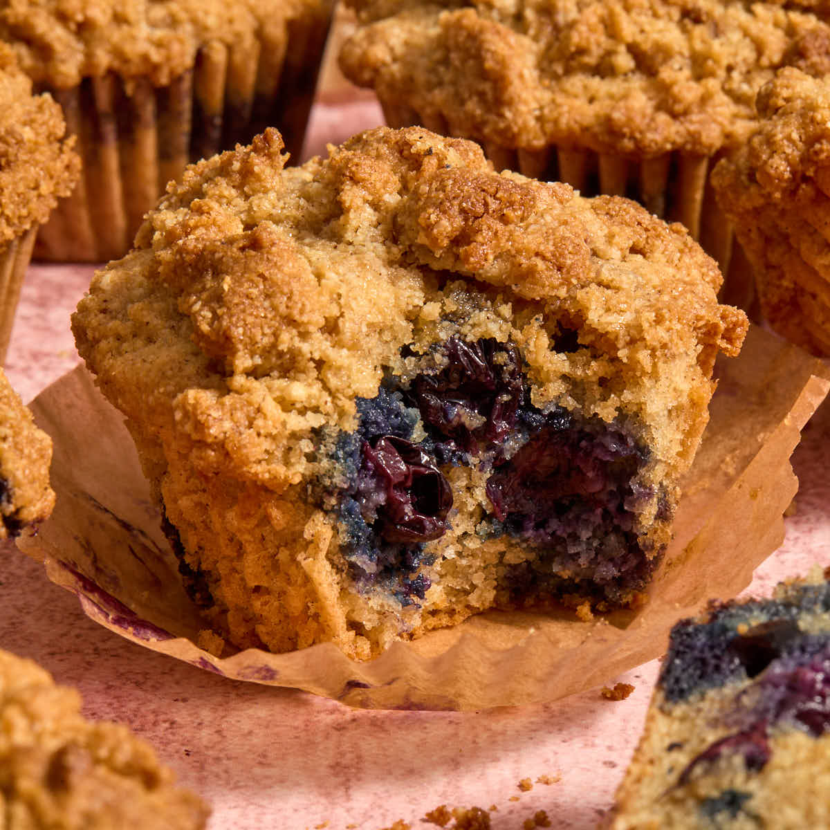 Almond flour blueberry coffee cake muffin with a bite removed and resting on a parchment muffin liner.