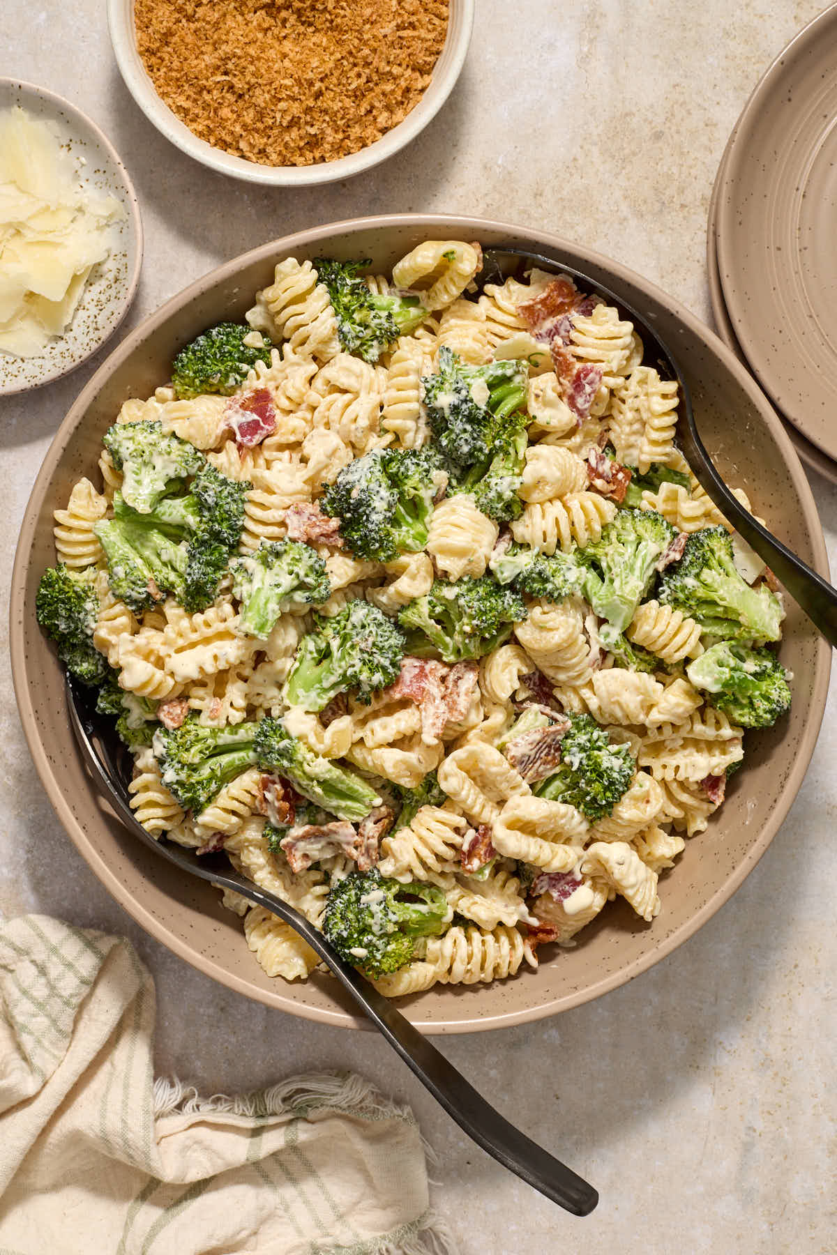 Broccoli pasta salad in a serving bowl with toasted breadcrumbs and shaved parmesan on the side.