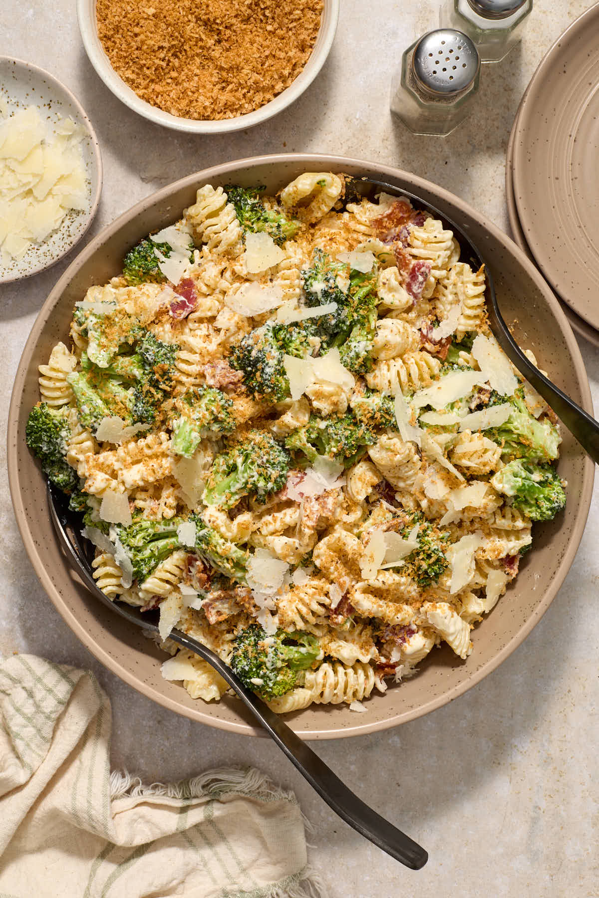 Broccoli caesar pasta salad in a beige bowl served with extra parmesan and toasted breadcrumbs.