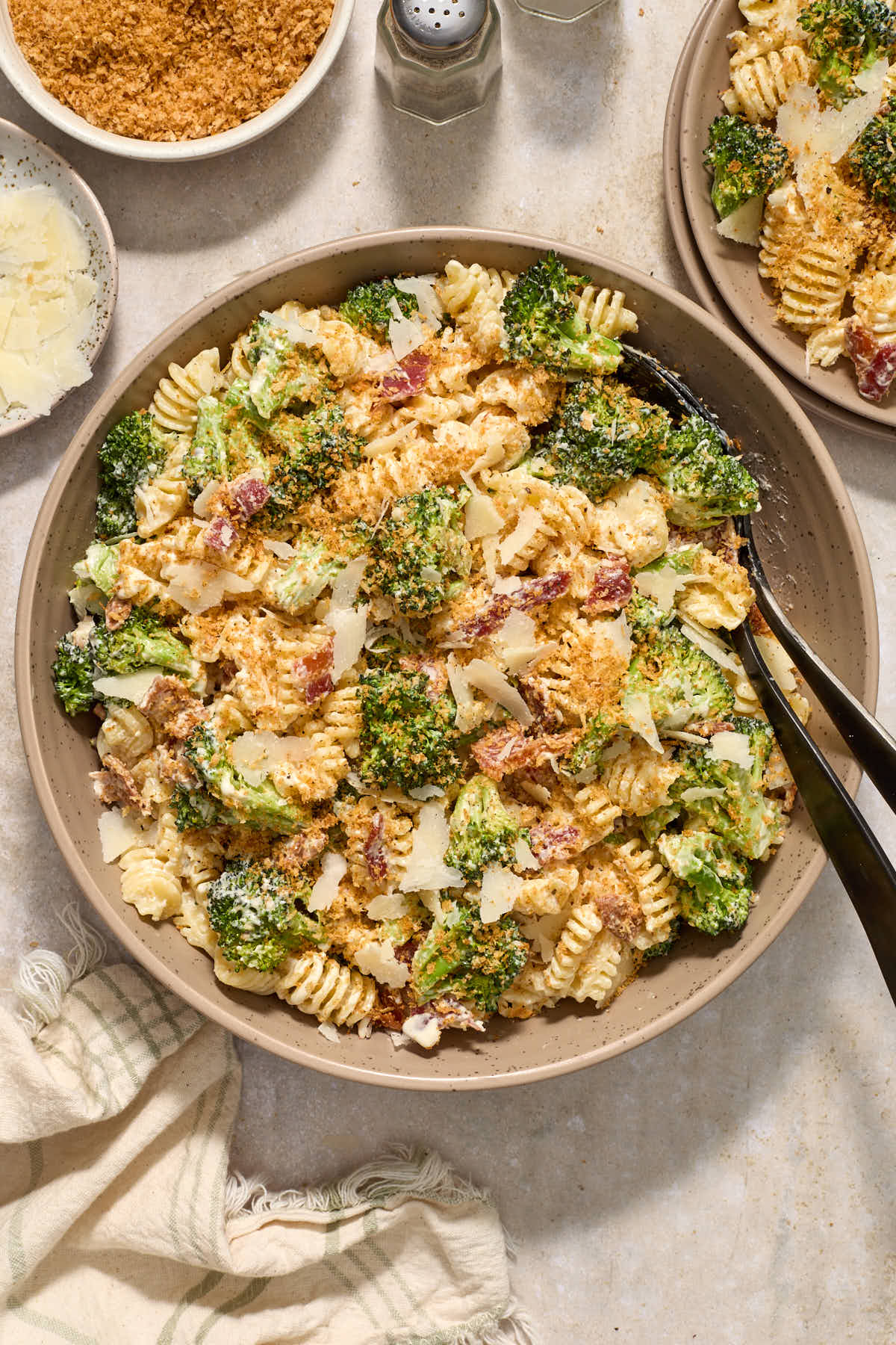 Pasta salad in a bowl with serving spoons and panko crumbs sprinkled over top.