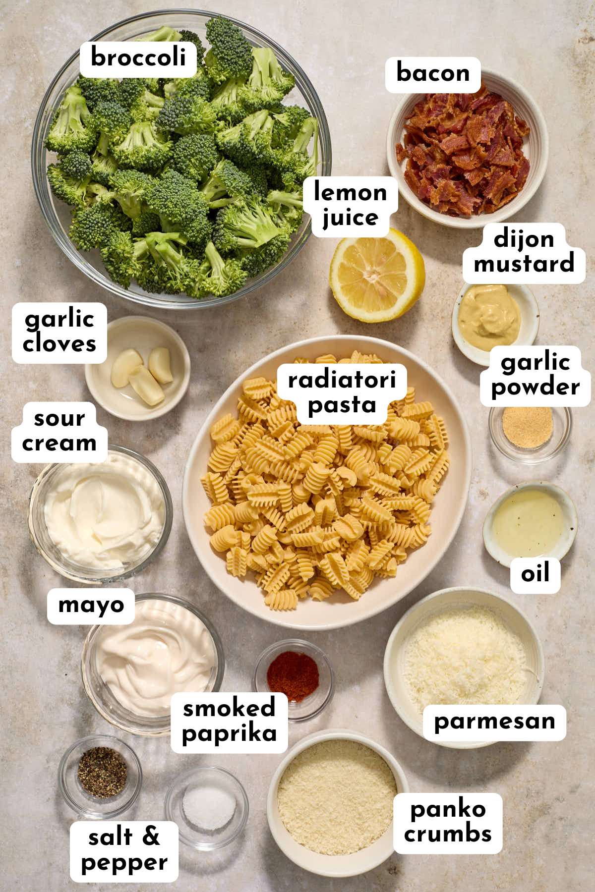 Ingredients to make a broccoli caesar pasta salad arranged individually and labeled.