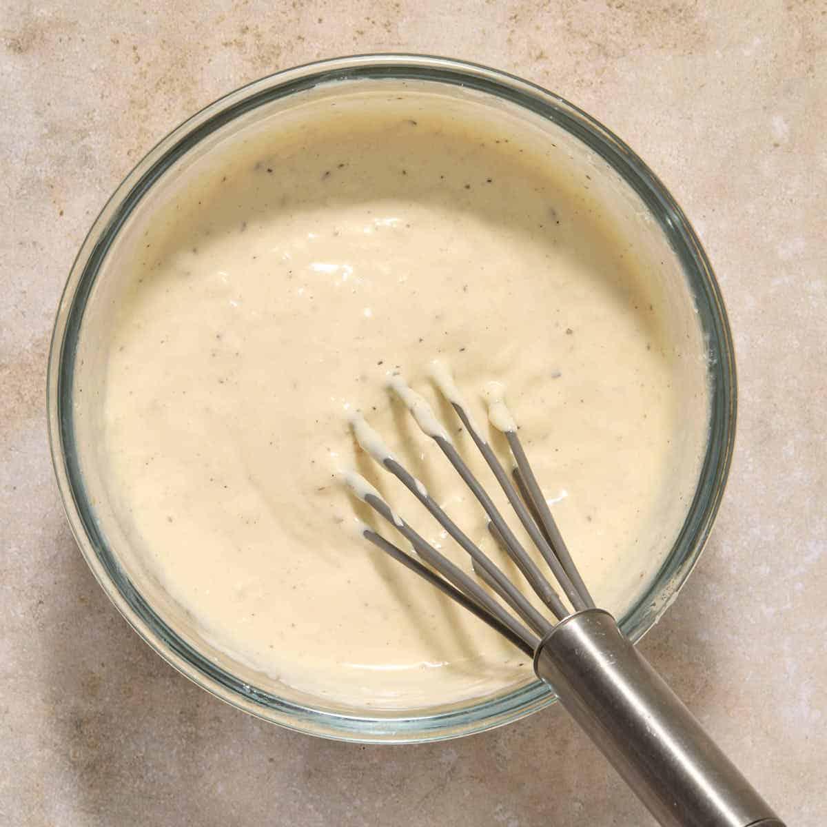 Caesar dressing mixed together in a small glass bowl with a whisk.