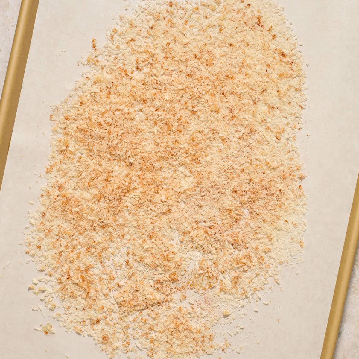 Untoasted panko crumbs spread out on a parchment lined baking sheet.