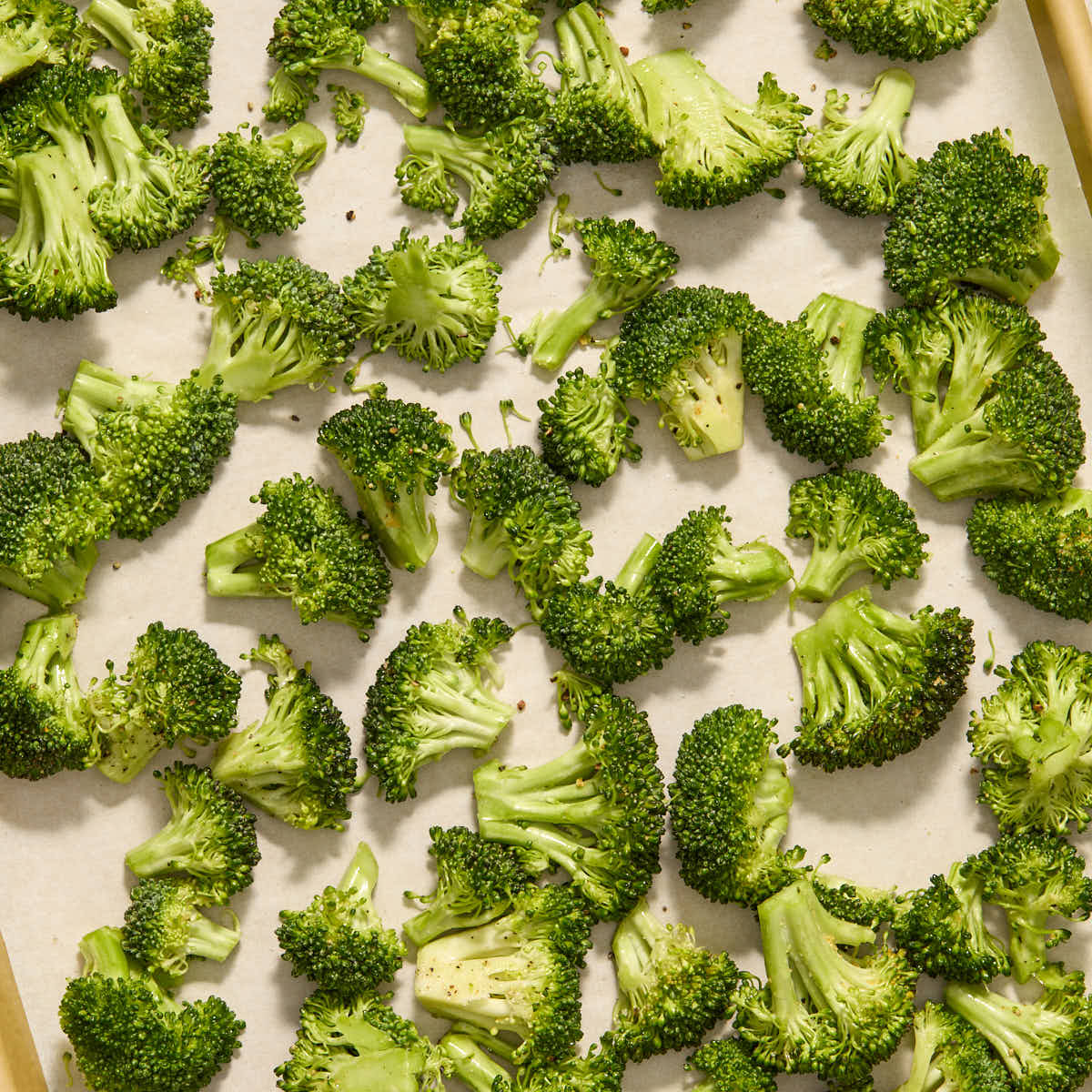 Raw, seasoned broccoli florets spread out on a baking sheet.